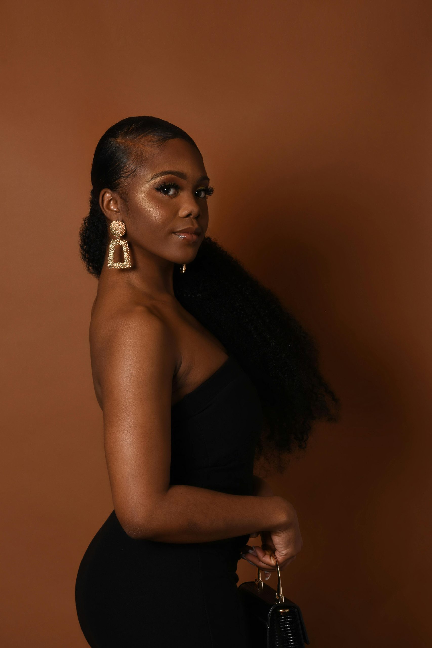 Stylish portrait of a young woman in a black dress against a brown background.